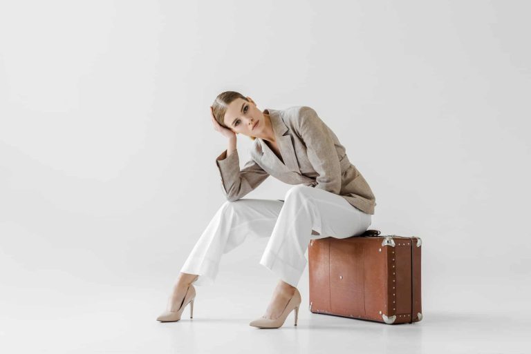 Women in linen jacket sitting on a suitcase