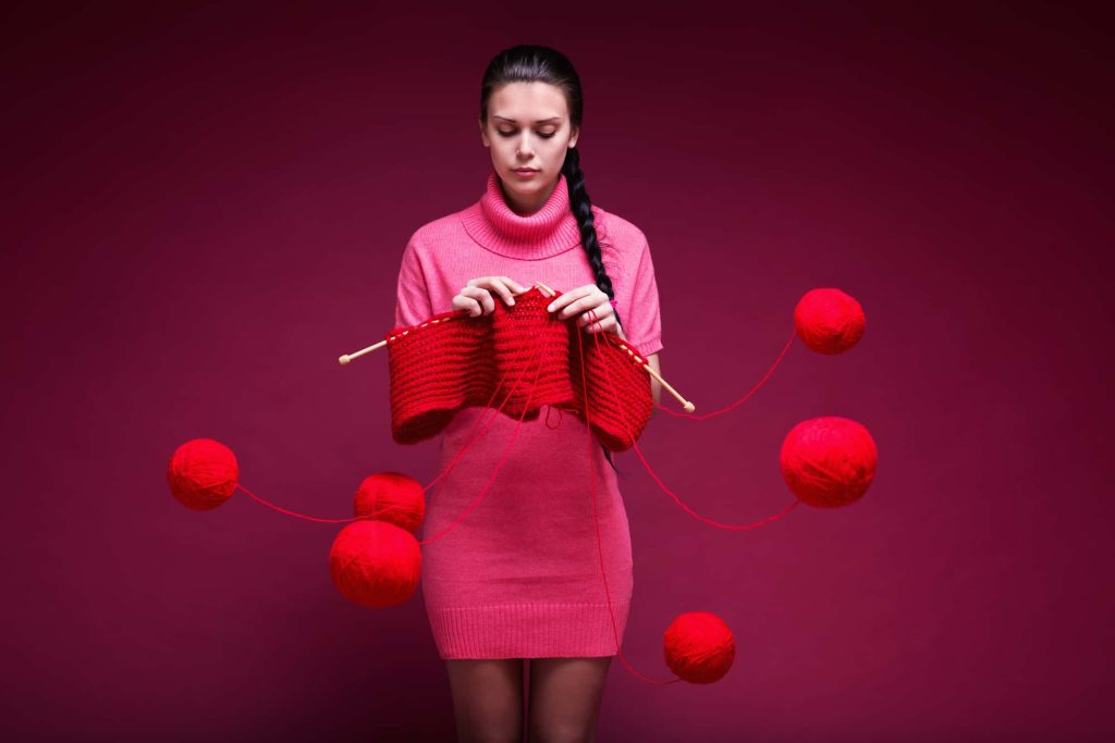 Young woman knits a scarf on a red background