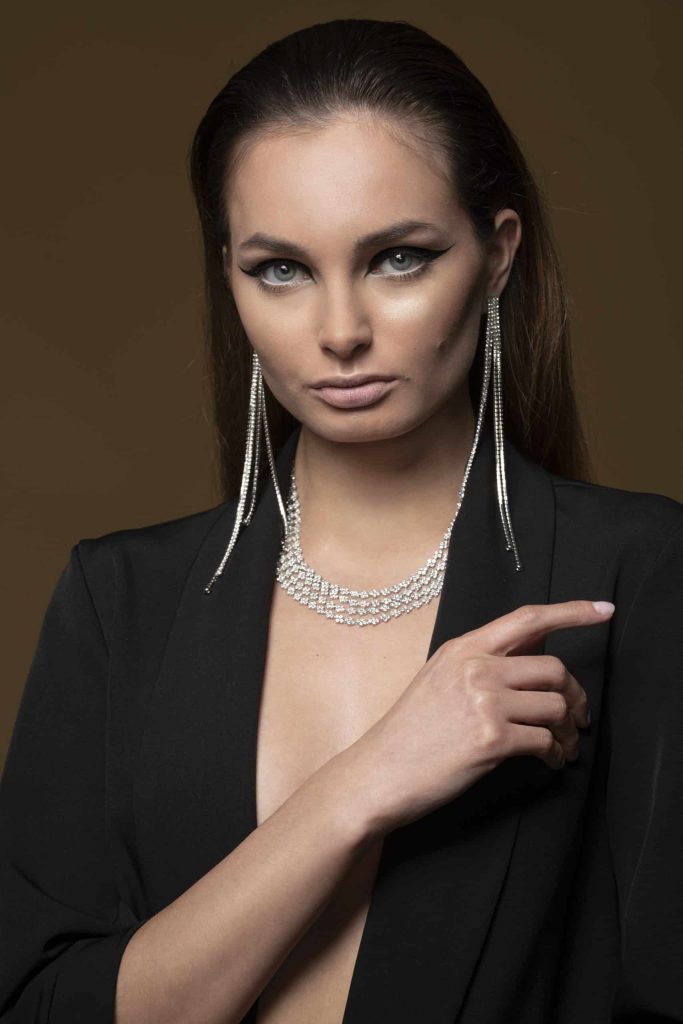 A woman with diamond jewellery, on dark beige background.